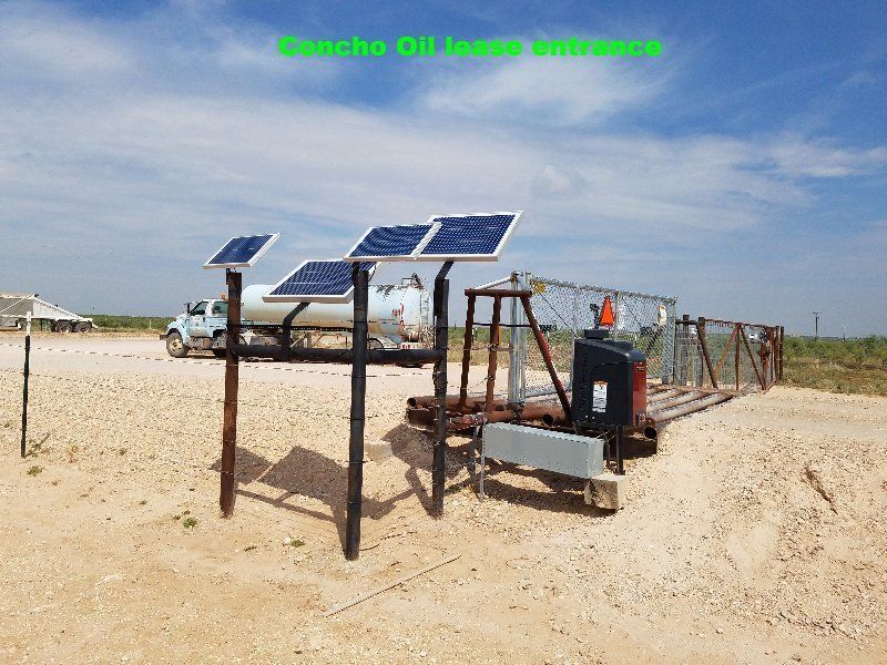 Solar panels on a metal frame at a remote sandy site under a blue sky.