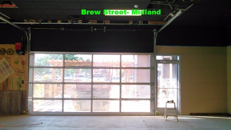 Empty storefront with large glass garage door and green “Brew Street Midland” sign above.