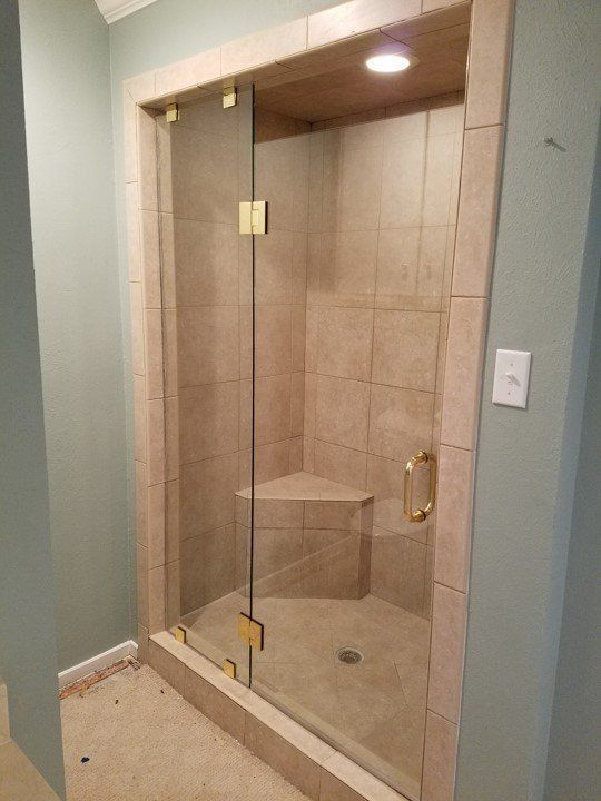 Glass-enclosed shower with beige tile, brass fixtures, and a built-in bench in a bathroom