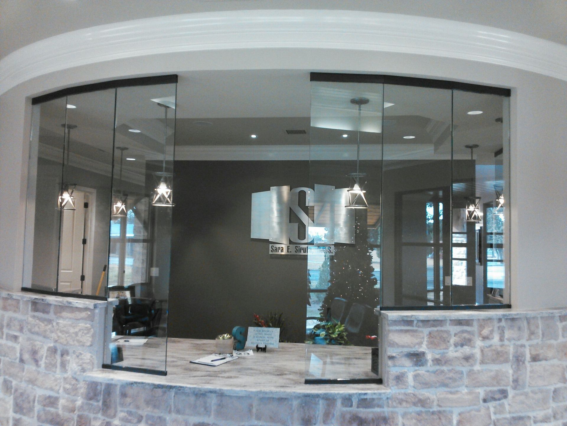 Modern kitchen viewed through a large arched pass-through window with pendant lights and stone half-wall.