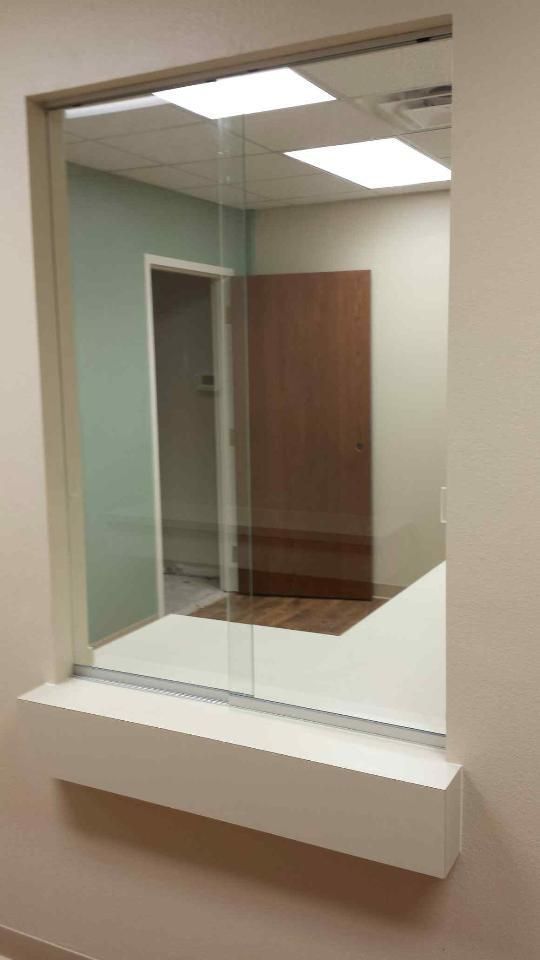 Interior office view through a glass window with a white sill, showing a wooden door and hallway.