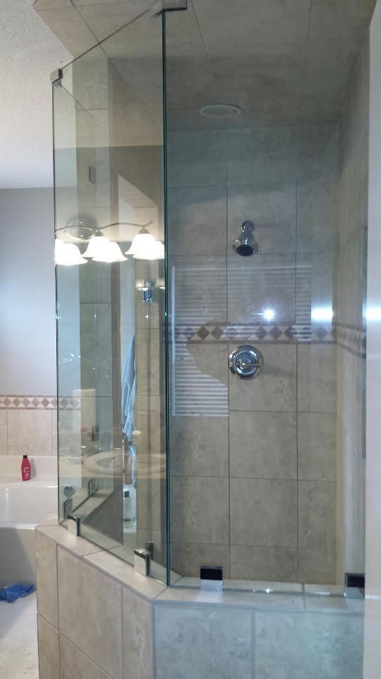 Glass-enclosed shower with beige tile walls and chrome fixtures in a bathroom.