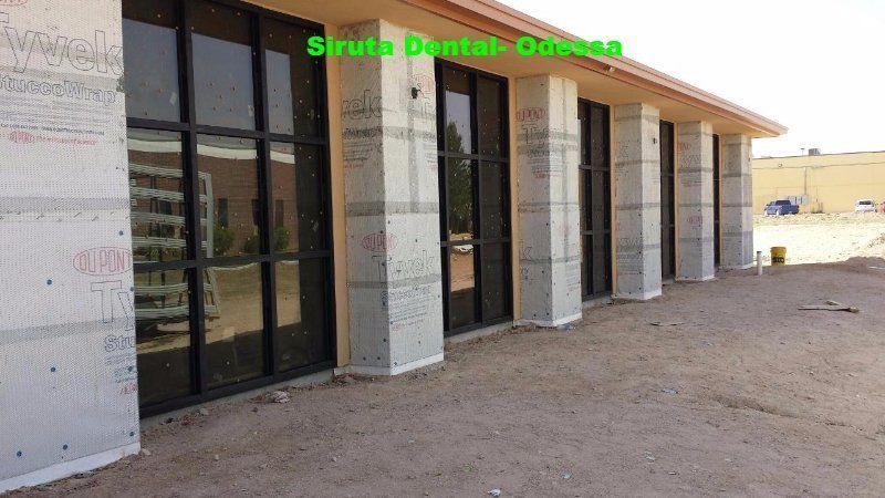 Exterior of a modern dental office with glass doors and white stone facade under construction