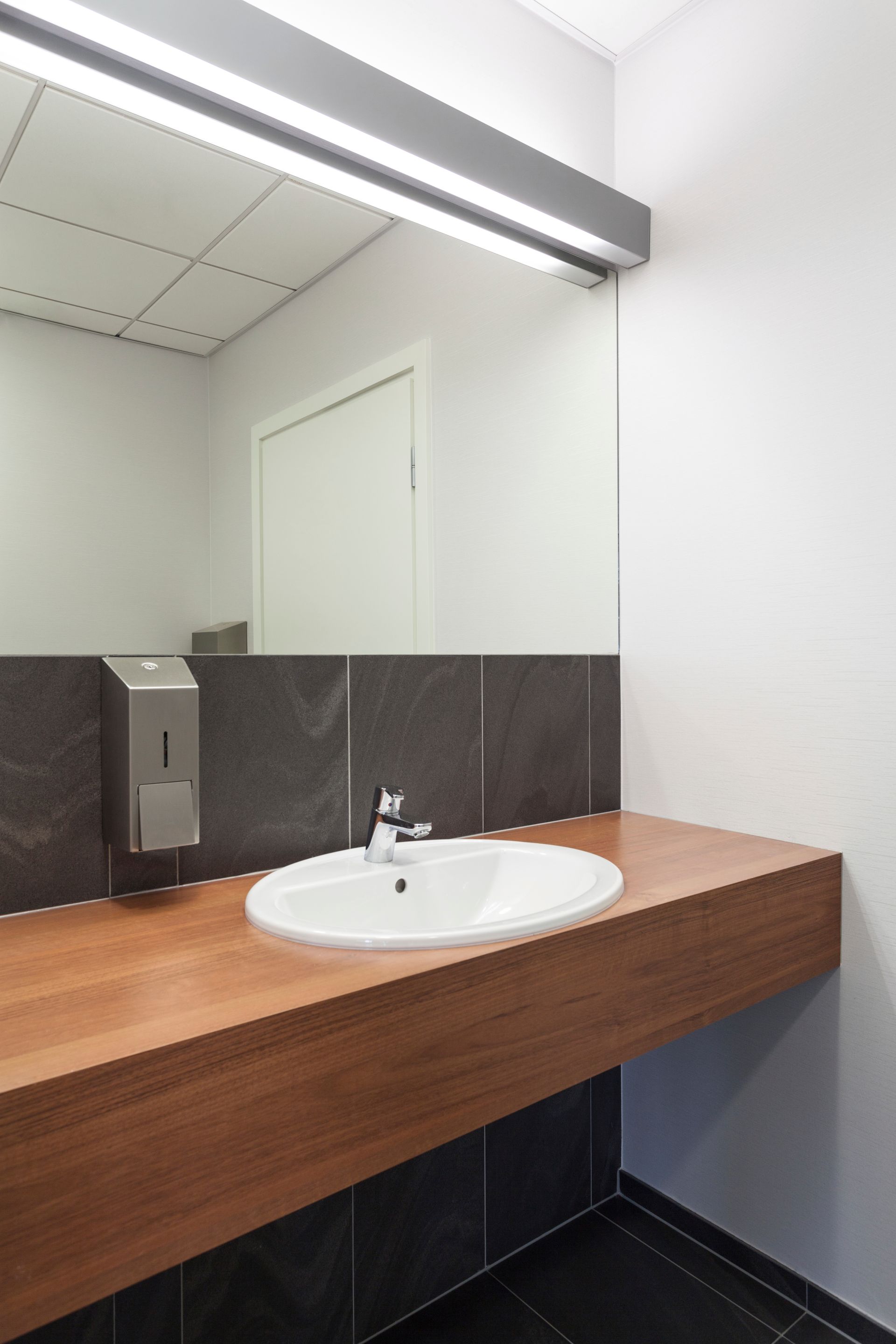 Modern bathroom sink with wooden countertop, large mirror, and dark tiled wall accents