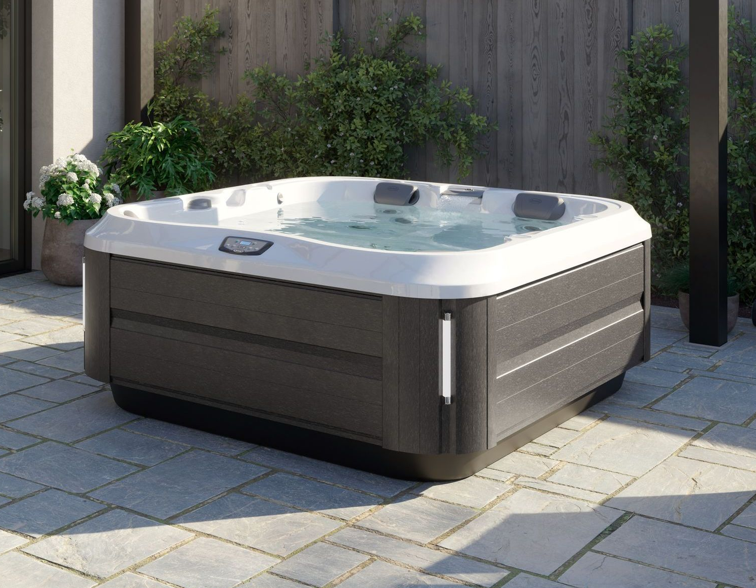 Gray hot tub on a patio beside a wooden fence, with plants and stone pavers.