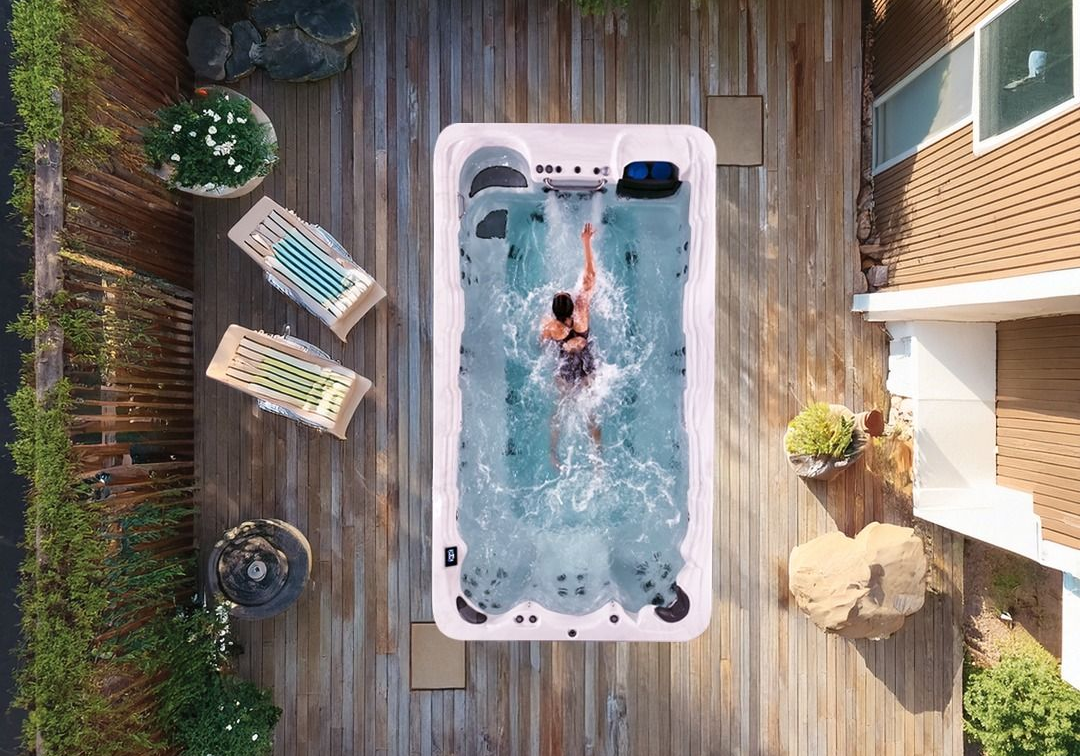 Overhead view of a person swimming in a small backyard pool beside wooden decking and lounge chairs