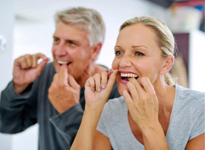 A man and a woman are flossing their teeth in front of a mirror.