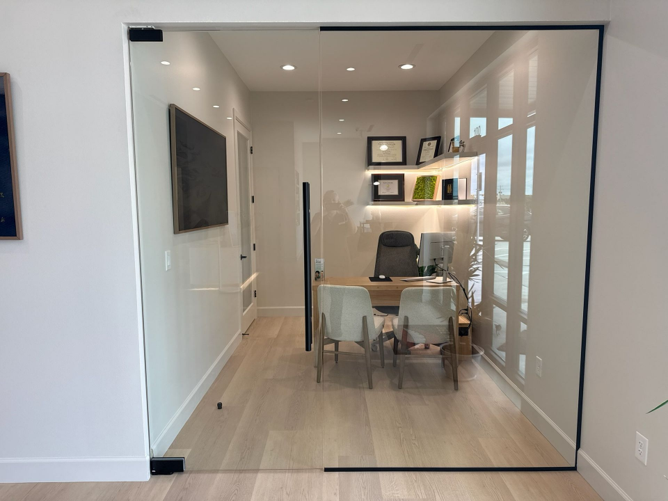 Modern office conference room with glass walls, a table, chairs, and wall shelves, viewed through an open doorway - Transcend Dental Office Photo