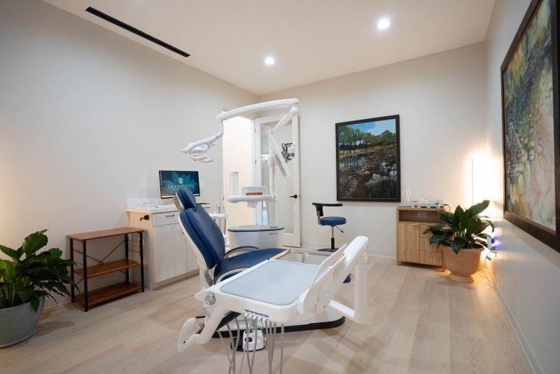 Bright dental exam room with chair, desk, monitor, and plants by a window - Transcend Dental Office Photo