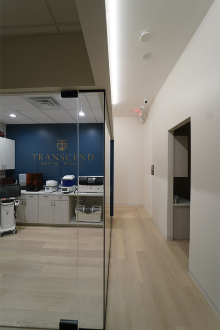 Modern office lobby with glass wall, blue reception desk, and hallway on the right - Transcend Dental Office Photo