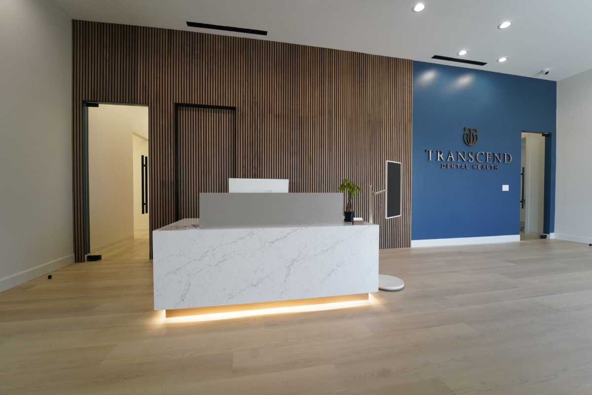 Modern lobby reception desk with wood slat wall, white marble front, and blue accent wall - Transcend Dental Office Photo