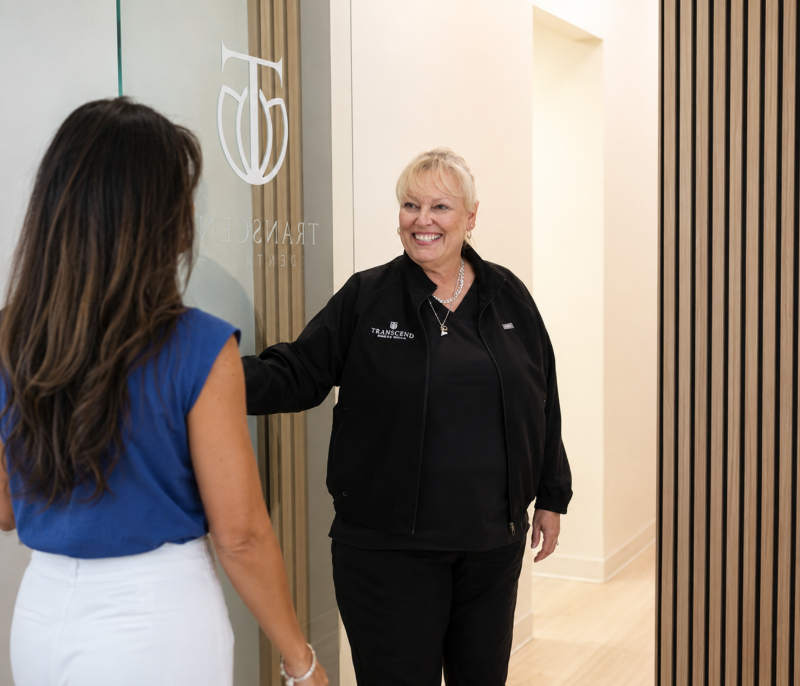 Two people greet each other at a doorway in a bright office lobby
