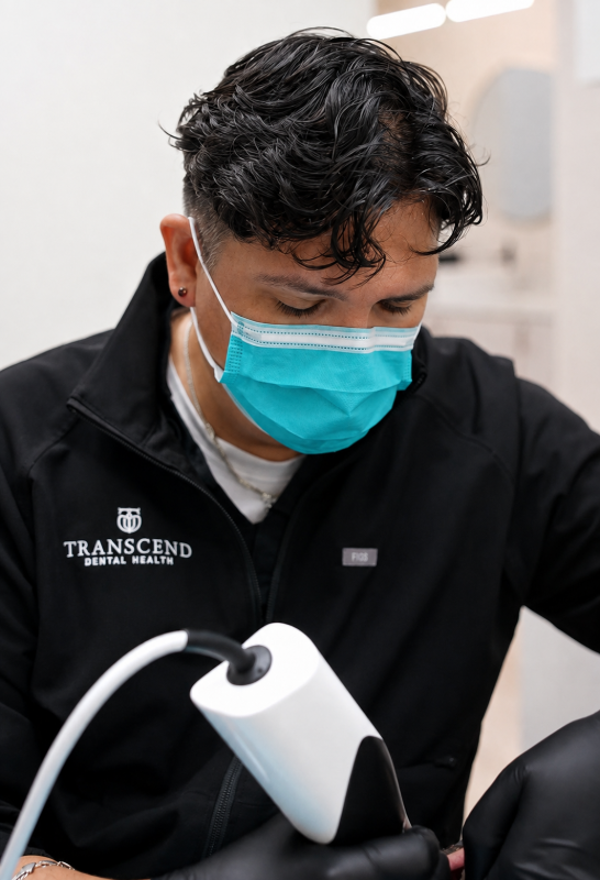Person in a black jacket and blue mask using a handheld device in a clinical setting