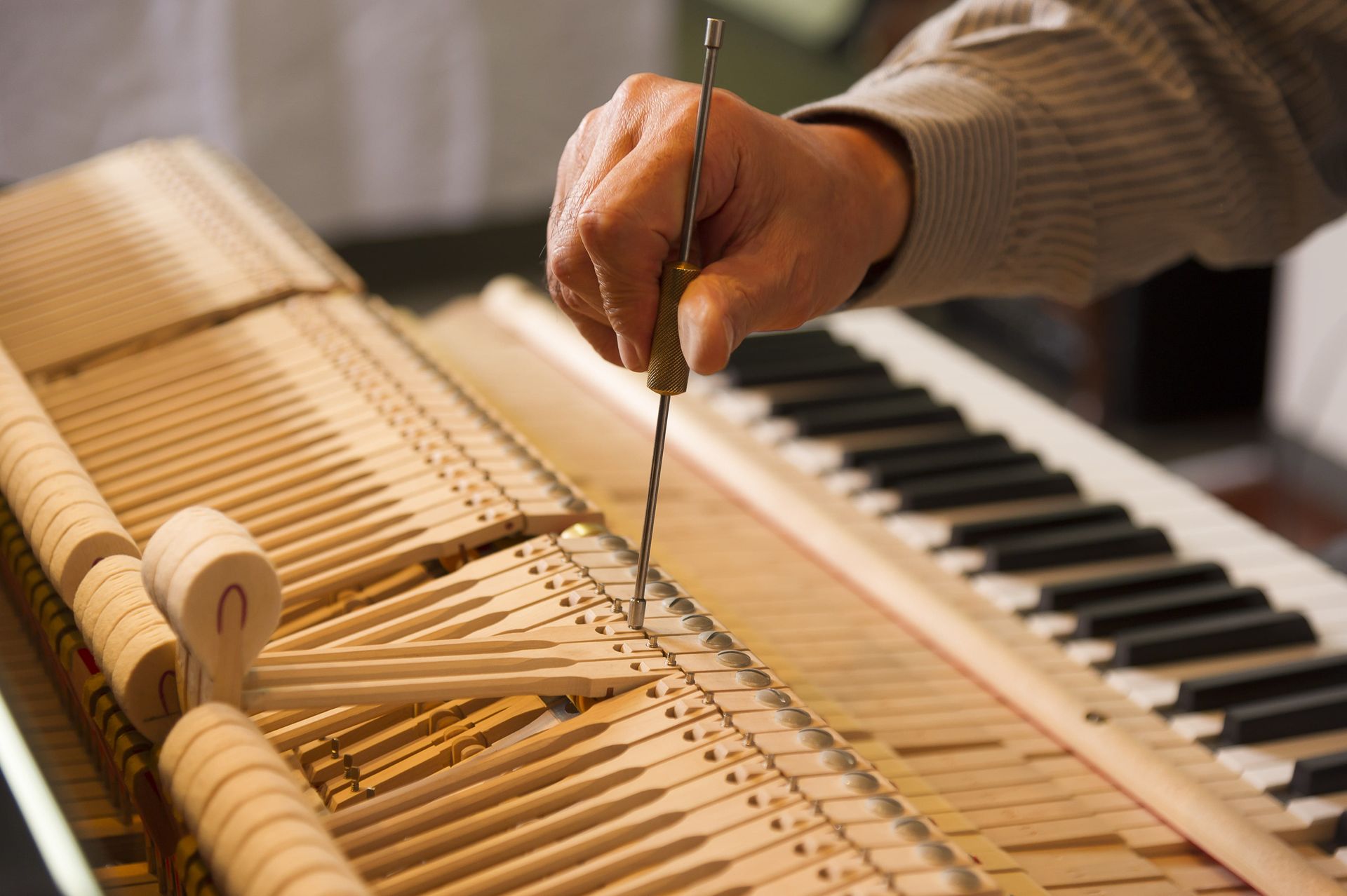 Hand tuning piano strings with a tool inside the instrument's open frame