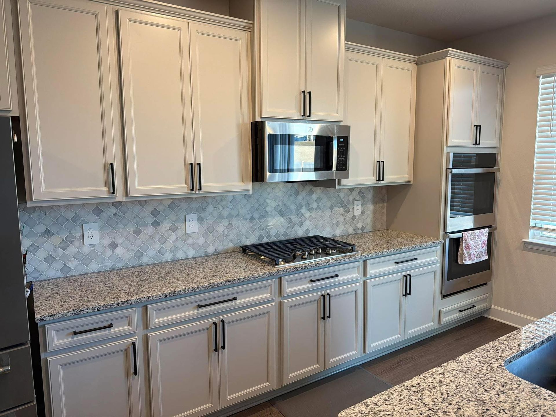 Modern kitchen with light wood cabinets, granite counters, mosaic backsplash, stainless steel appliances, and gas range.