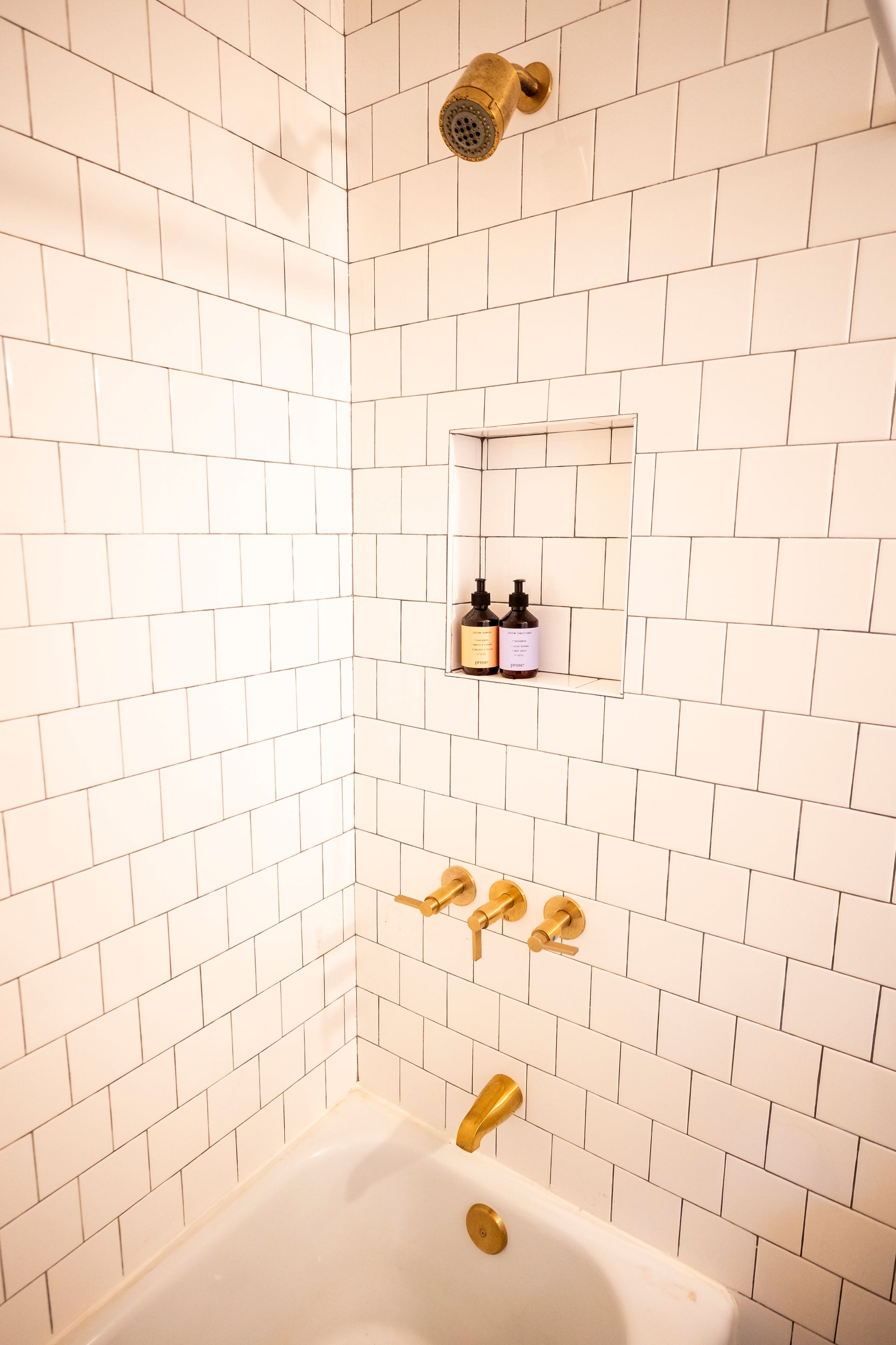 A bathroom with white tiles , a bathtub and a shower.