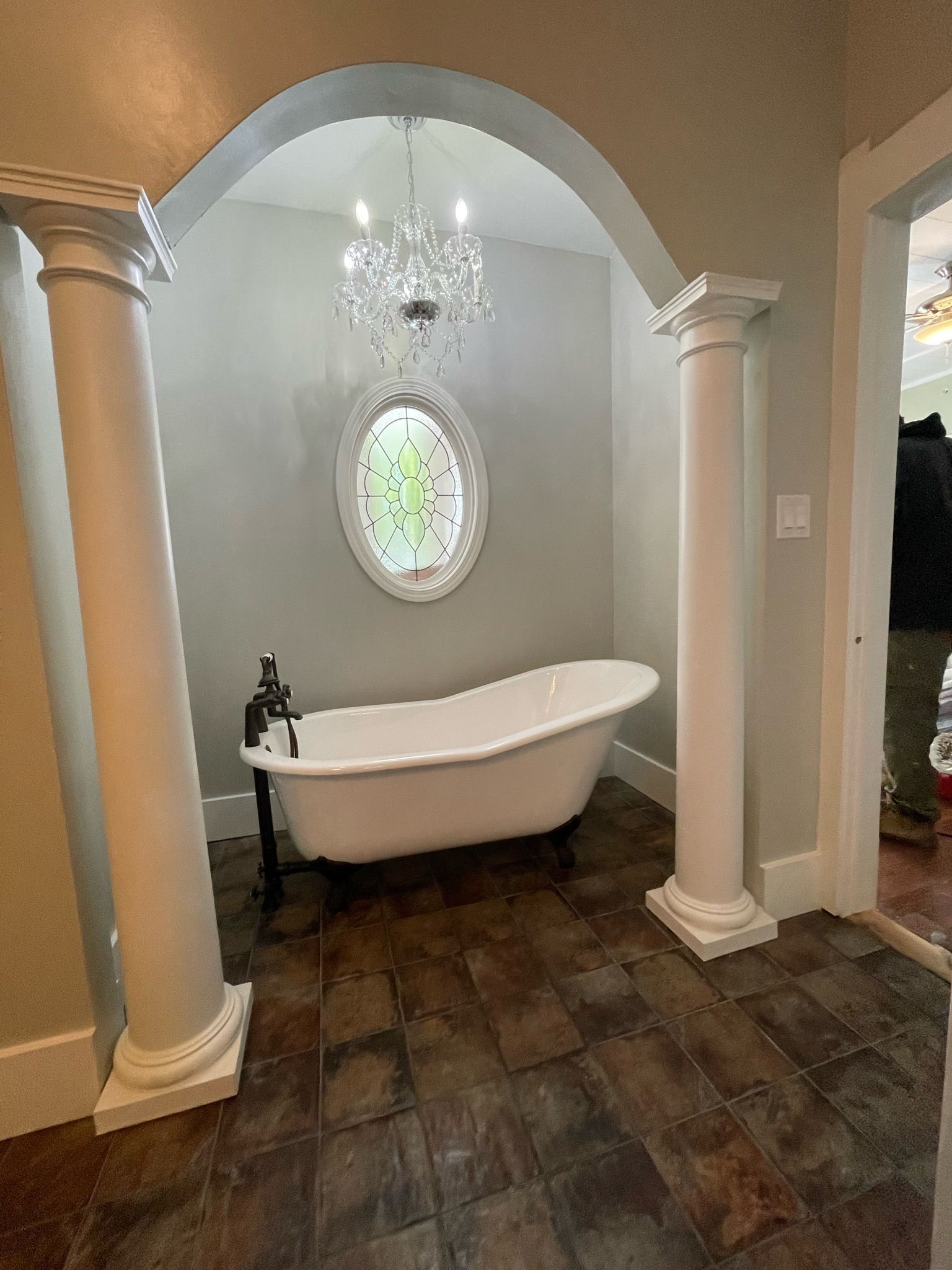 A clawfoot bathtub sits under an arched alcove with a hanging chandelier -BittnerSweet Co