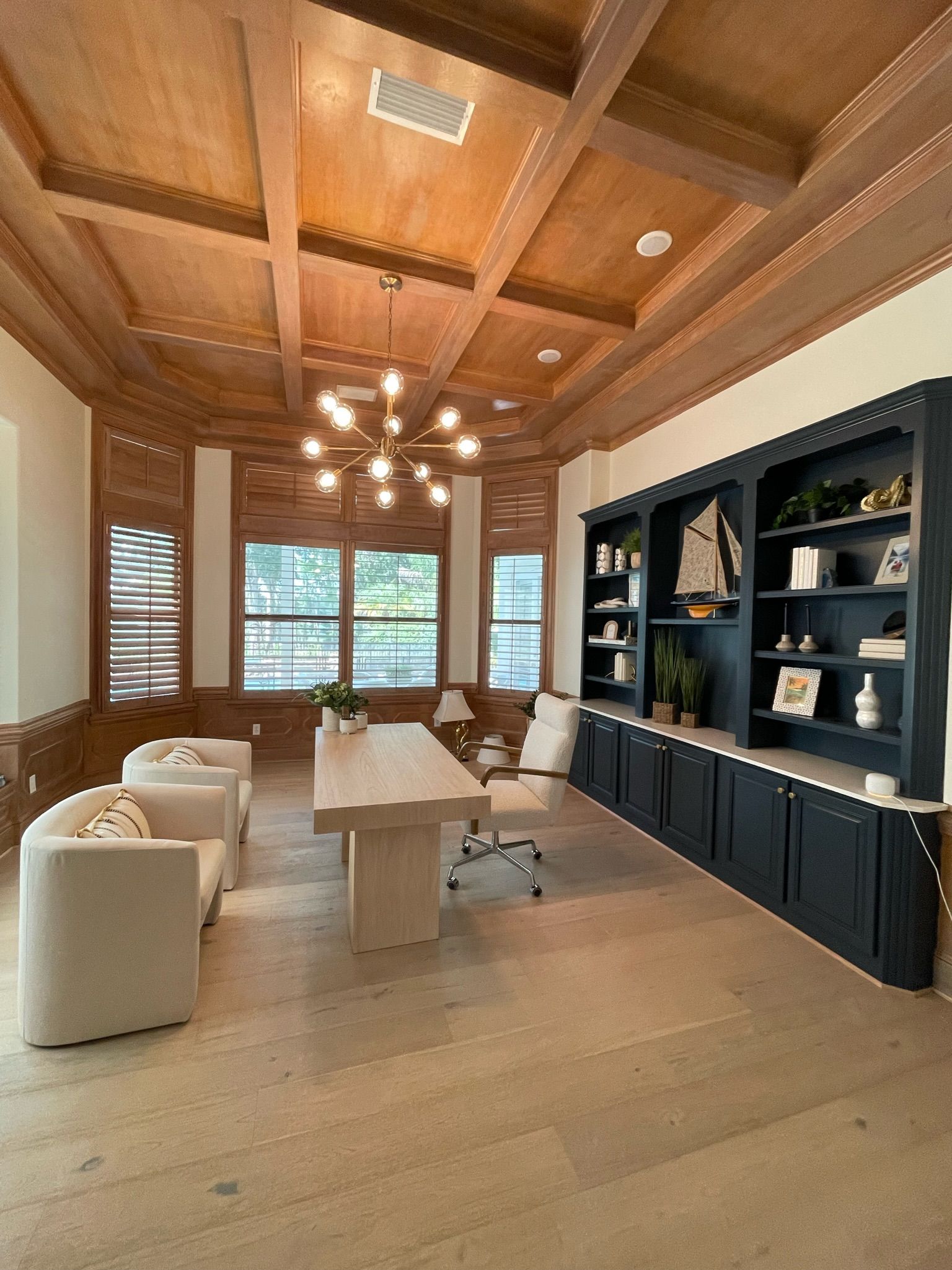 Bright living room with wood ceiling, white seating, dining table, and built-in shelving by a large window. - BittnerSweet Co.