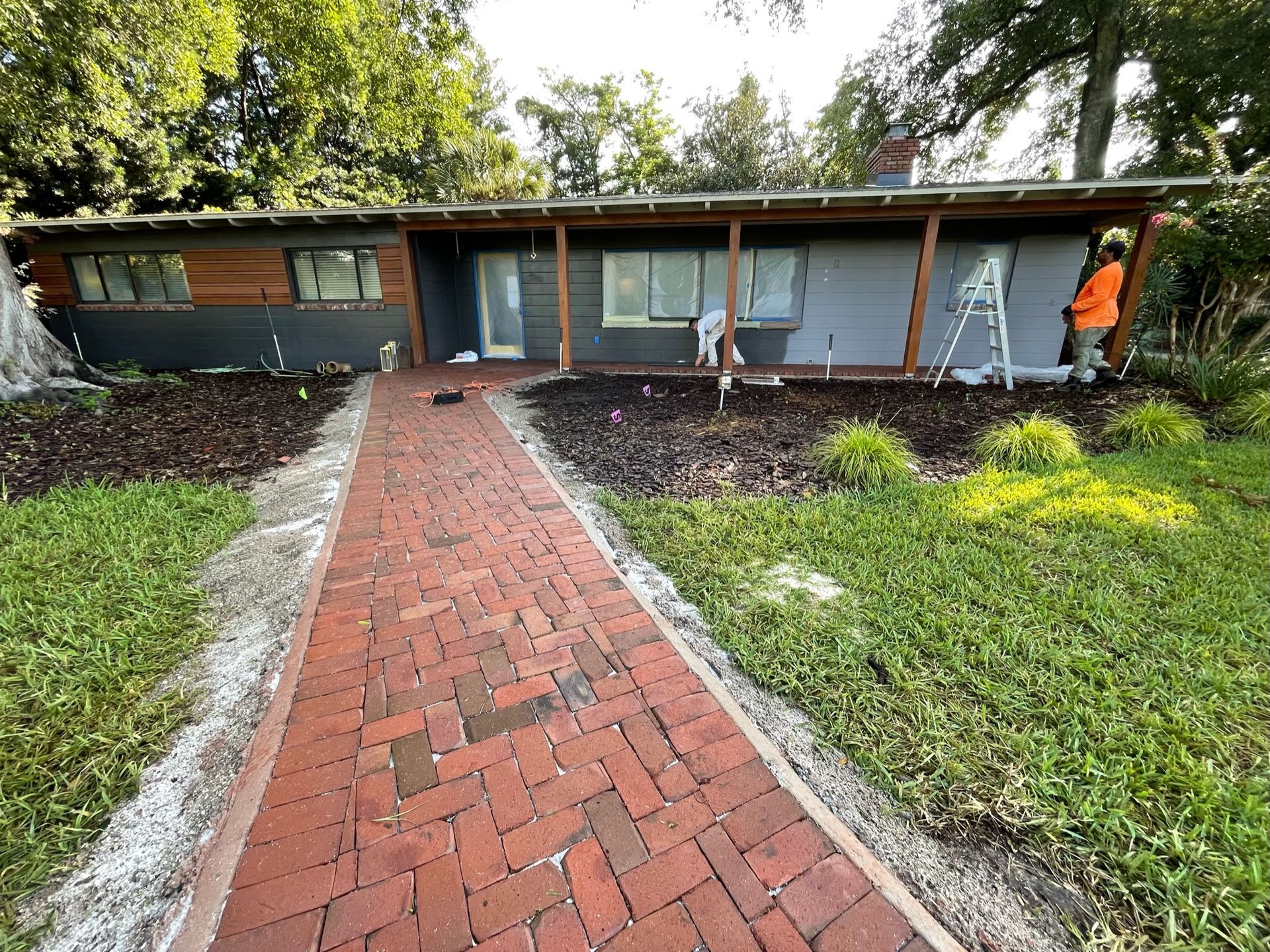 Brick walkway leading to a low modern house with large windows and a green yard - BittnerSweet Co