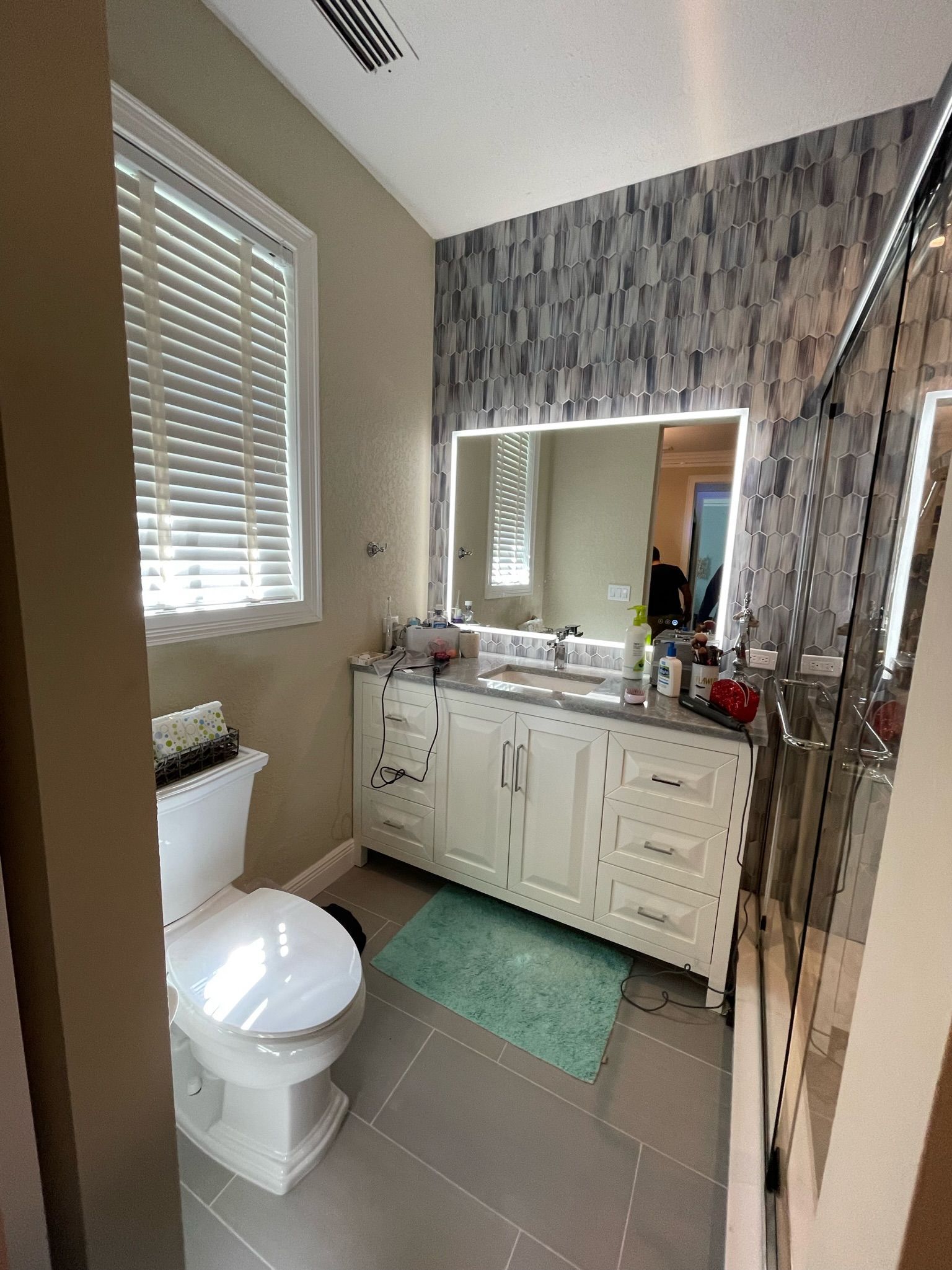 Small bathroom with toilet, vanity sink, mirror, tiled floor, and turquoise bath mat.