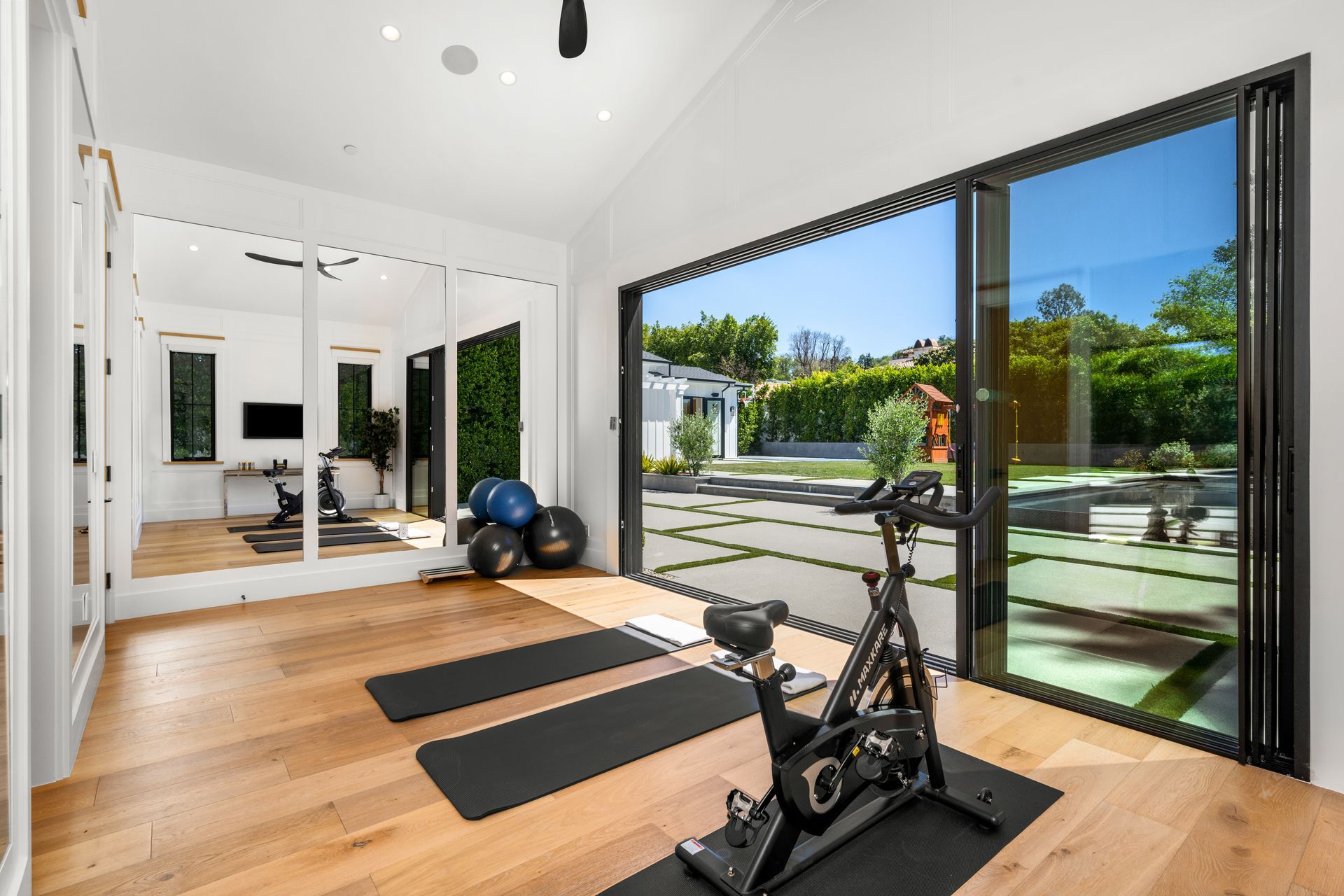 Bright home gym with exercise bike, yoga mats, and floor-to-ceiling windows overlooking a sunny patio - BIttnerSweet Co.