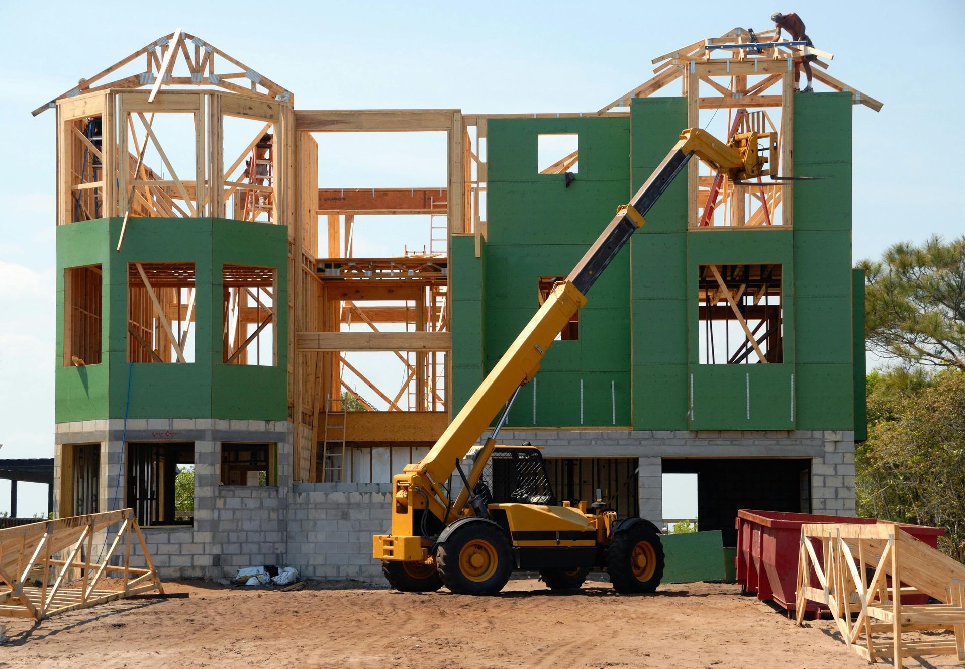 A large house is being built with a yellow forklift in front of it