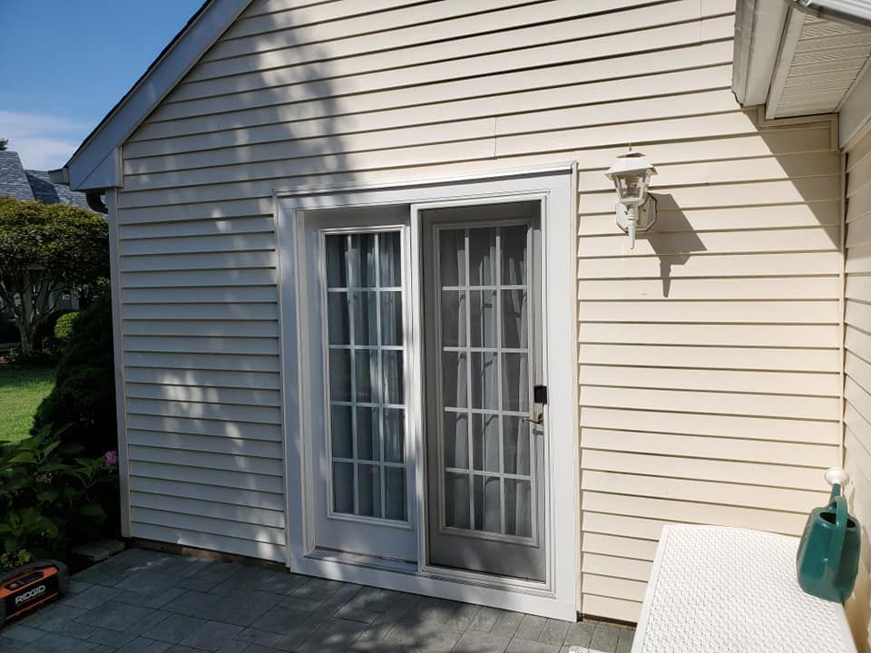 A sliding glass door with a white frame set in light beige vinyl siding, next to an outdoor wall light and green pitcher.
