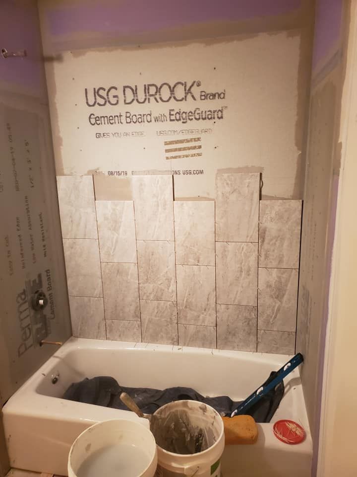 A partially tiled shower surround with white stone-look tiles installed over USG Durock cement board above a bathtub.