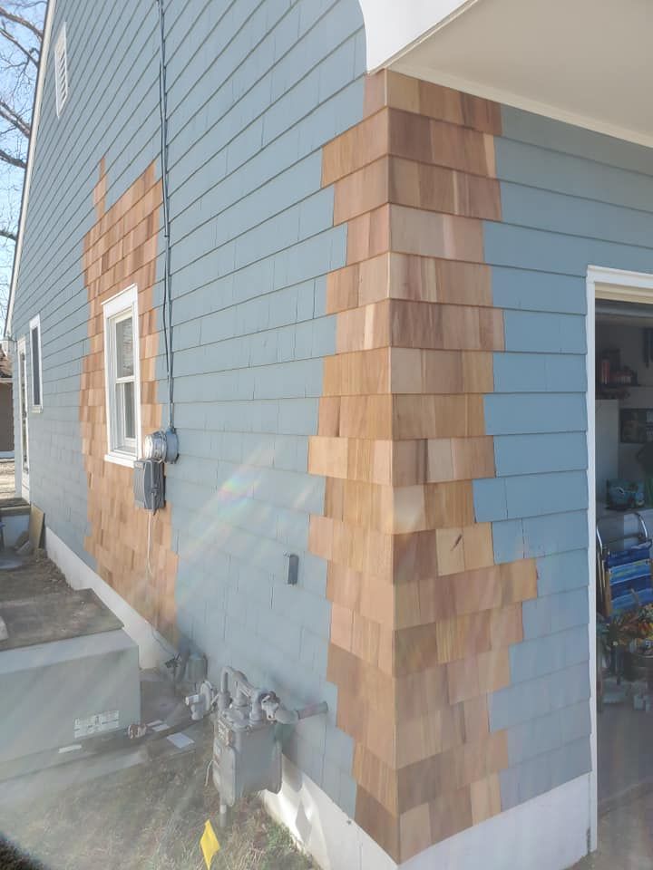 A house exterior featuring blue horizontal siding accented with patches of unpainted, natural wood shingles on the corners.