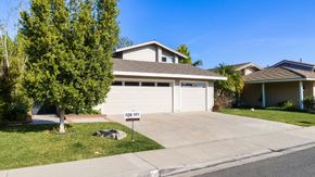 A suburban single-story house with a three-car garage, large front lawn, a tree on the left, and a driveway.