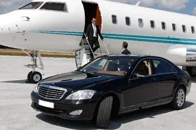 Black car parked near a private jet as a suited man exits with another.