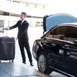Man in suit loading luggage into black car trunk.