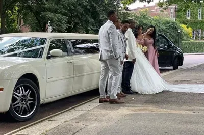 Wedding party next to a white limousine; bride in white gown, bridesmaids in pink dresses.