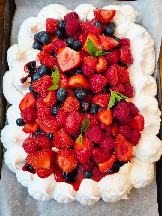 Berry-topped pavlova with strawberries, raspberries, blueberries, and whipped cream around the edge
