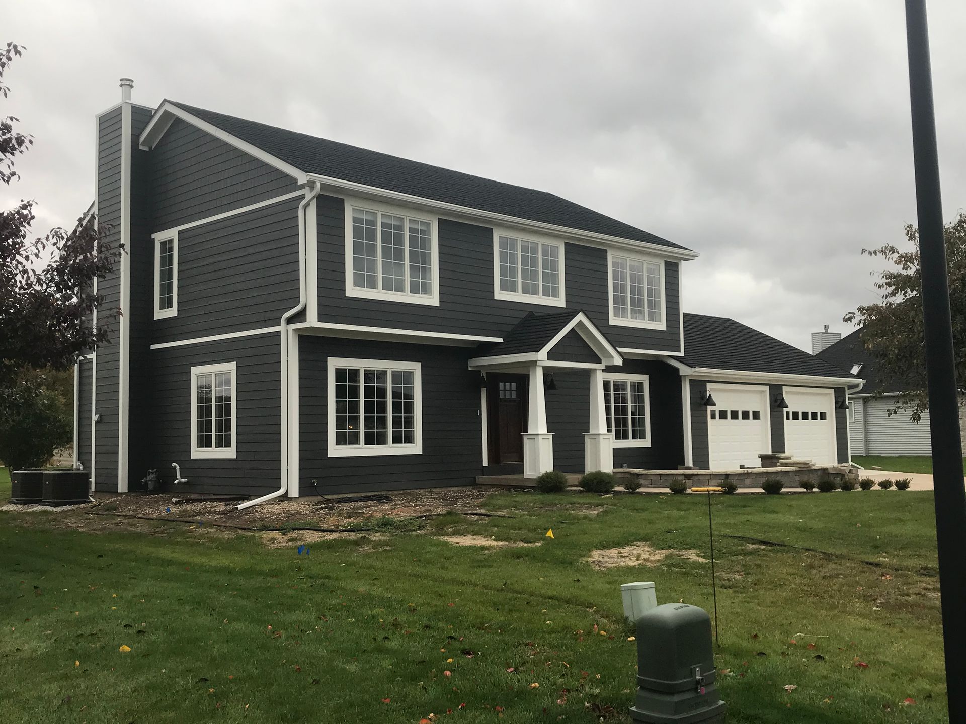 Two-story house with dark gray siding, white trim, and a black roof on a cloudy day.