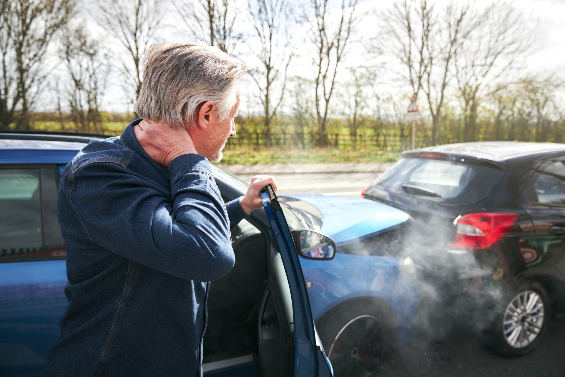 Senior man with whiplash getting out of his car after a traffic accident