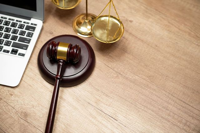 Laptop, gavel, and scales of justice on a wooden desk Laptop, gavel, and scales of justice on a wooden desk