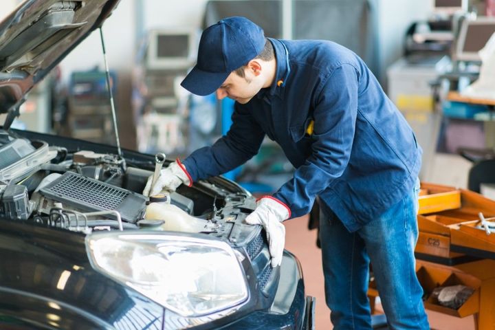Mechanic in blue uniform inspecting a car engine in an auto repair shop