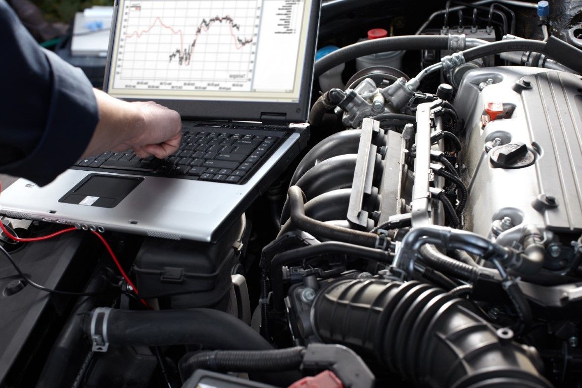 Mechanic using a laptop to diagnose a car engine in an open hood bay