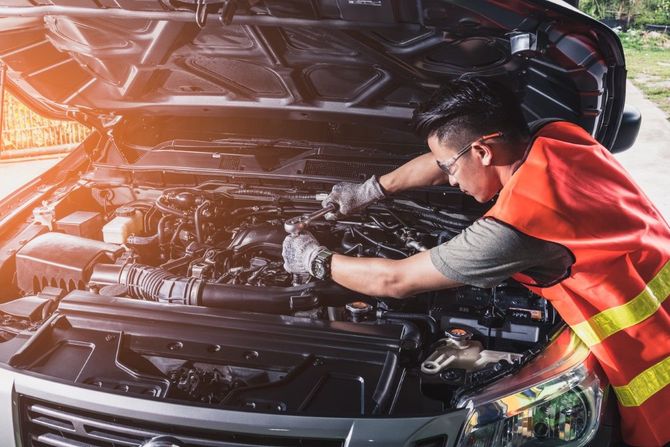 Mechanic in orange safety vest working on a car engine with the hood open in a garage