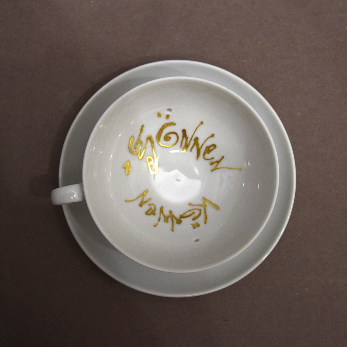 Titel: Gönnen können
Ansicht von oben.
Die Plastik der Künstlerin Benita von Wendt besteht aus einer durchlöcherten Tasse,  die auf einer Untertasse steht. In der Tasse ist der Schriftzug 