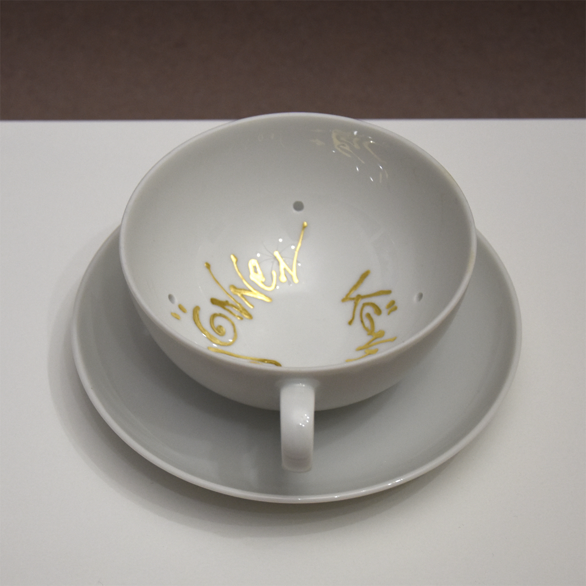 Titel: Gönnen können
Ansicht seitlich von oben.
Die Plastik der Künstlerin Benita von Wendt besteht aus einer durchlöcherten Tasse,  die auf einer Untertasse steht. In der Tasse ist der Schriftzug 