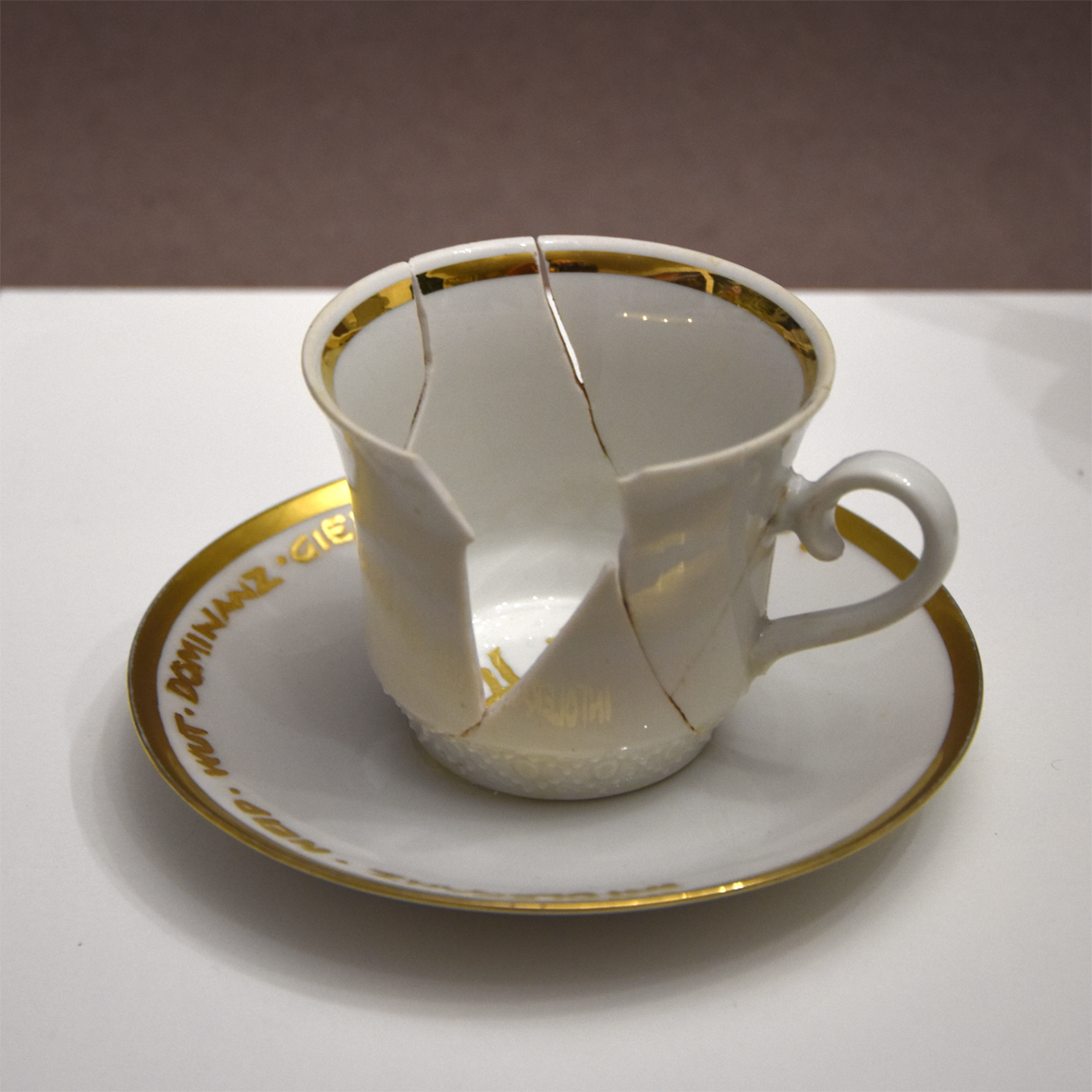 Titel: Zu spät
Ansicht Detail Tasse seitlich.
Die Plastik der Künstlerin Benita von Wendt besteht
aus einer Tasse der ein großes Stück Porzellan fehlt. In der Tasse steht der Schriftzug Hass mit Blattgold geschrieben. Daneben steht ein Kännchen, das von Innen beleuchtet ist. Innen befindet sich der Schriftzug Toleranz.