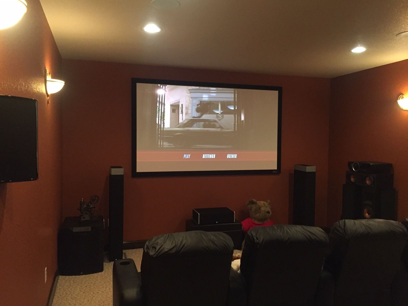 A home theater with a large screen and a teddy bear sitting in front of it.