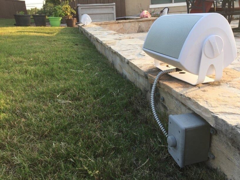 A white speaker is sitting on a stone wall next to a lawn.