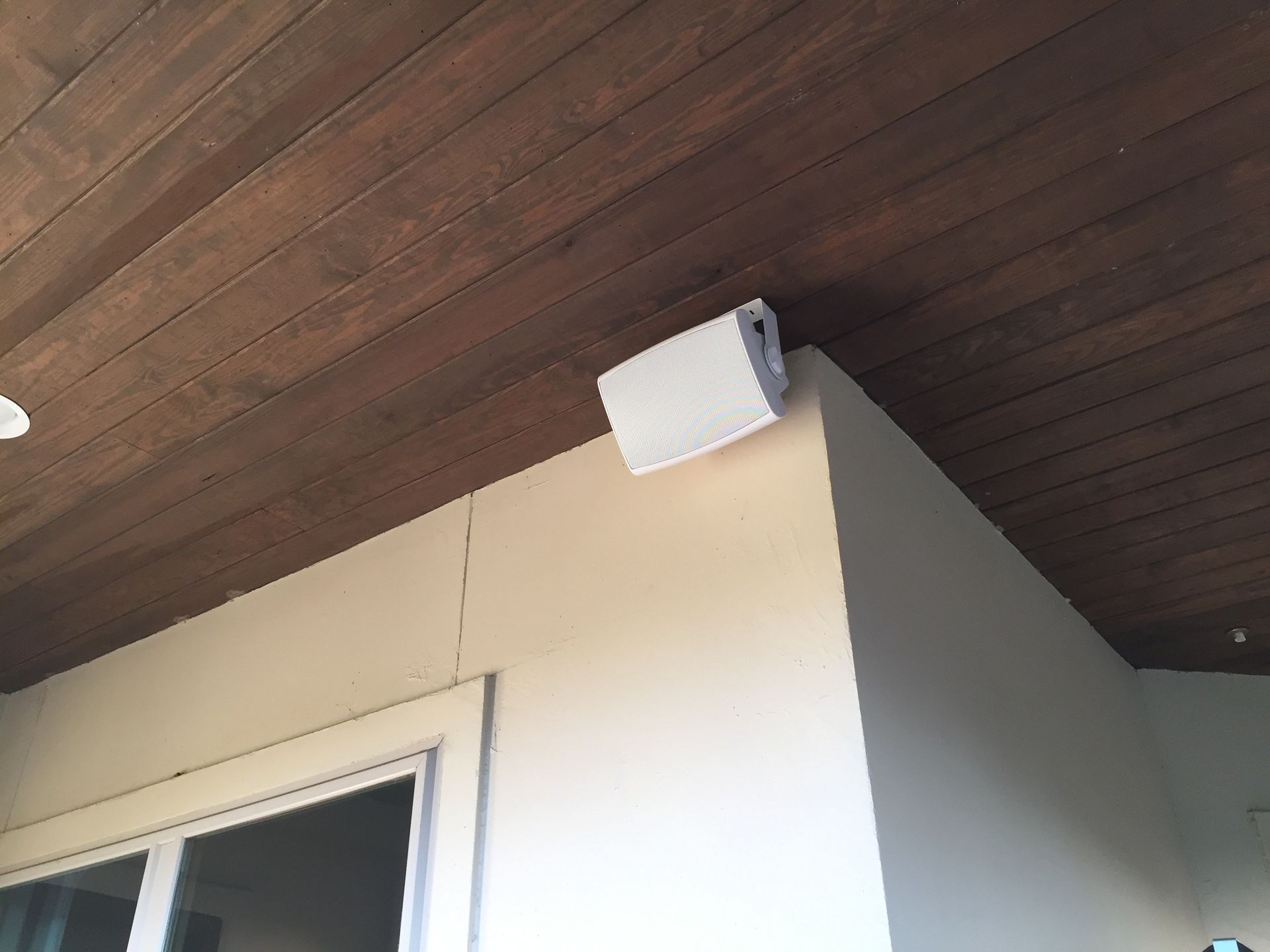 A white speaker is hanging from the ceiling of a room.