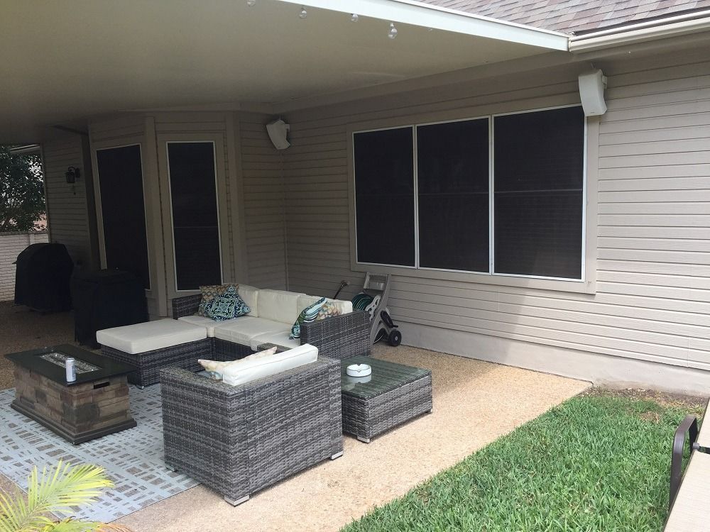 A patio with a couch , chairs and a table in front of a house.