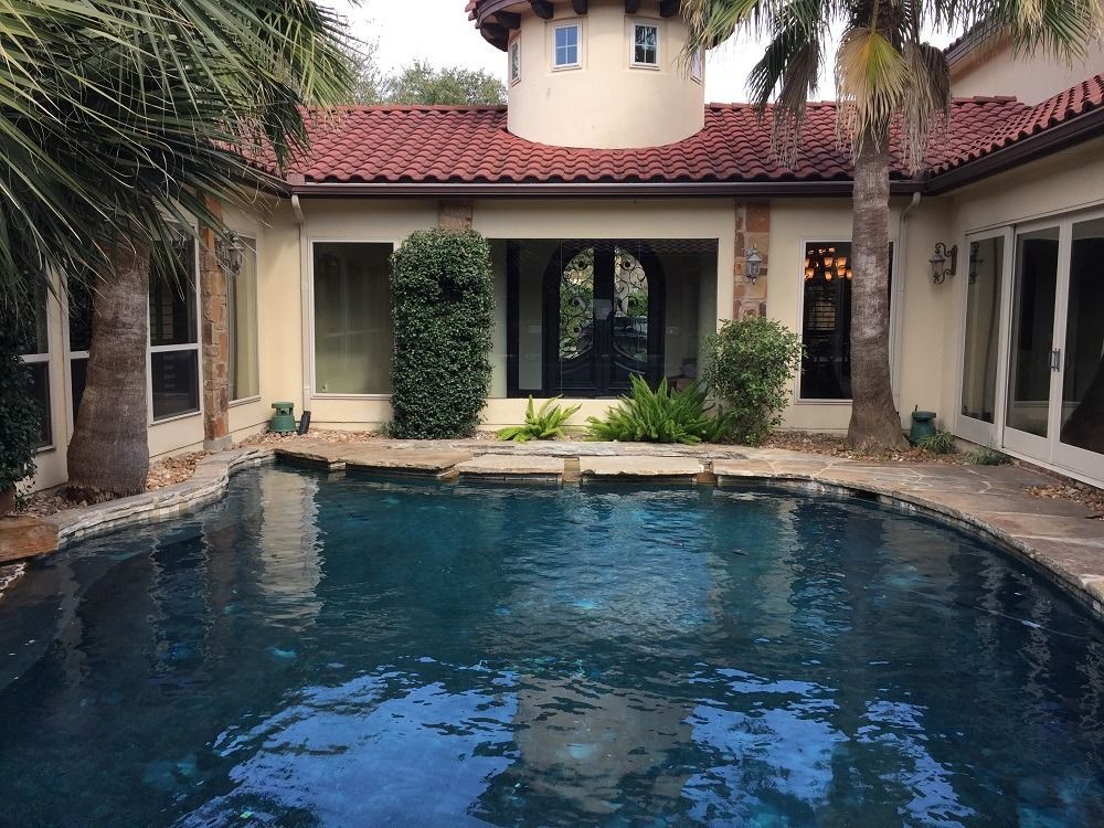 A large swimming pool in the backyard of a house surrounded by palm trees.