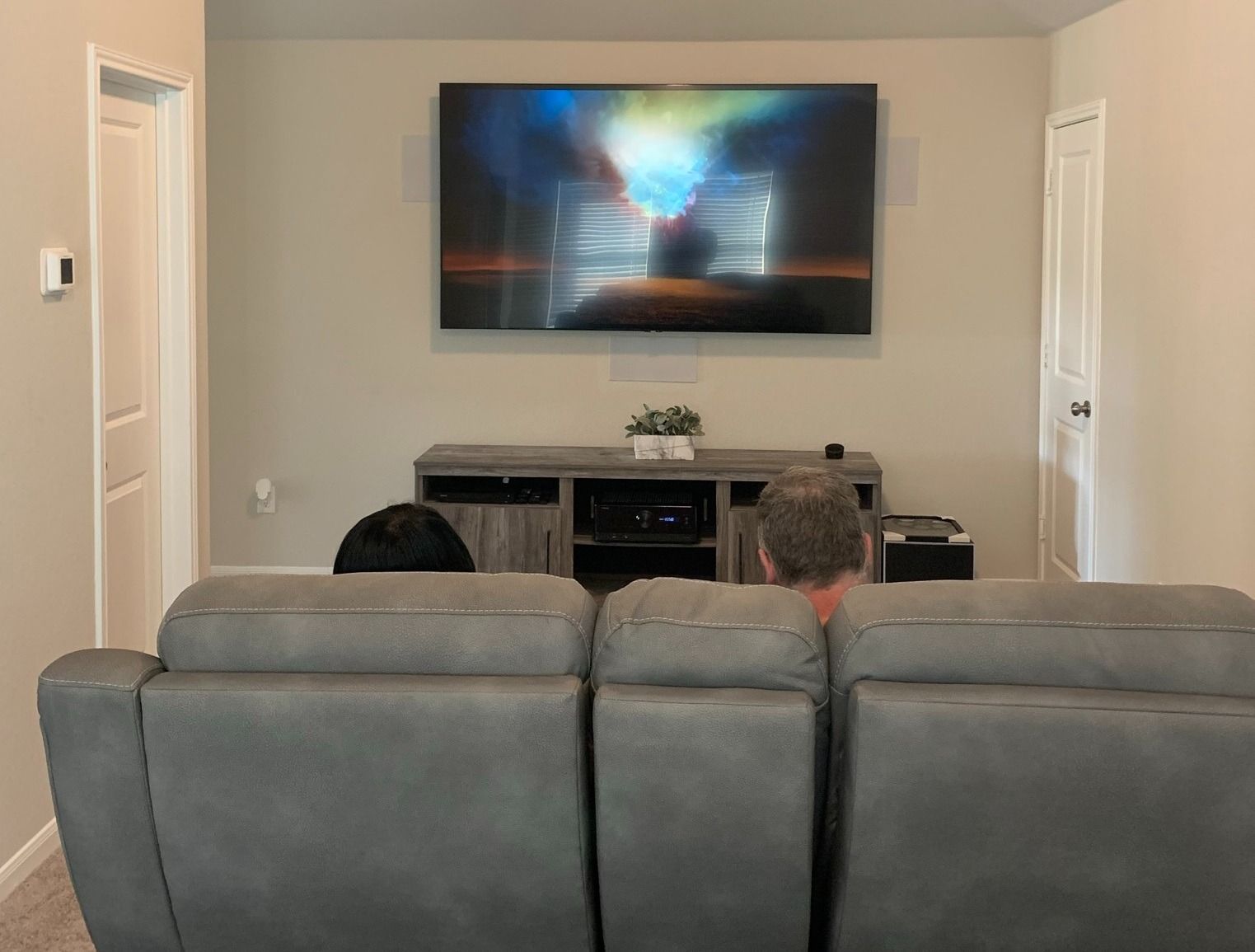 A man is sitting on a couch in a living room watching a television.