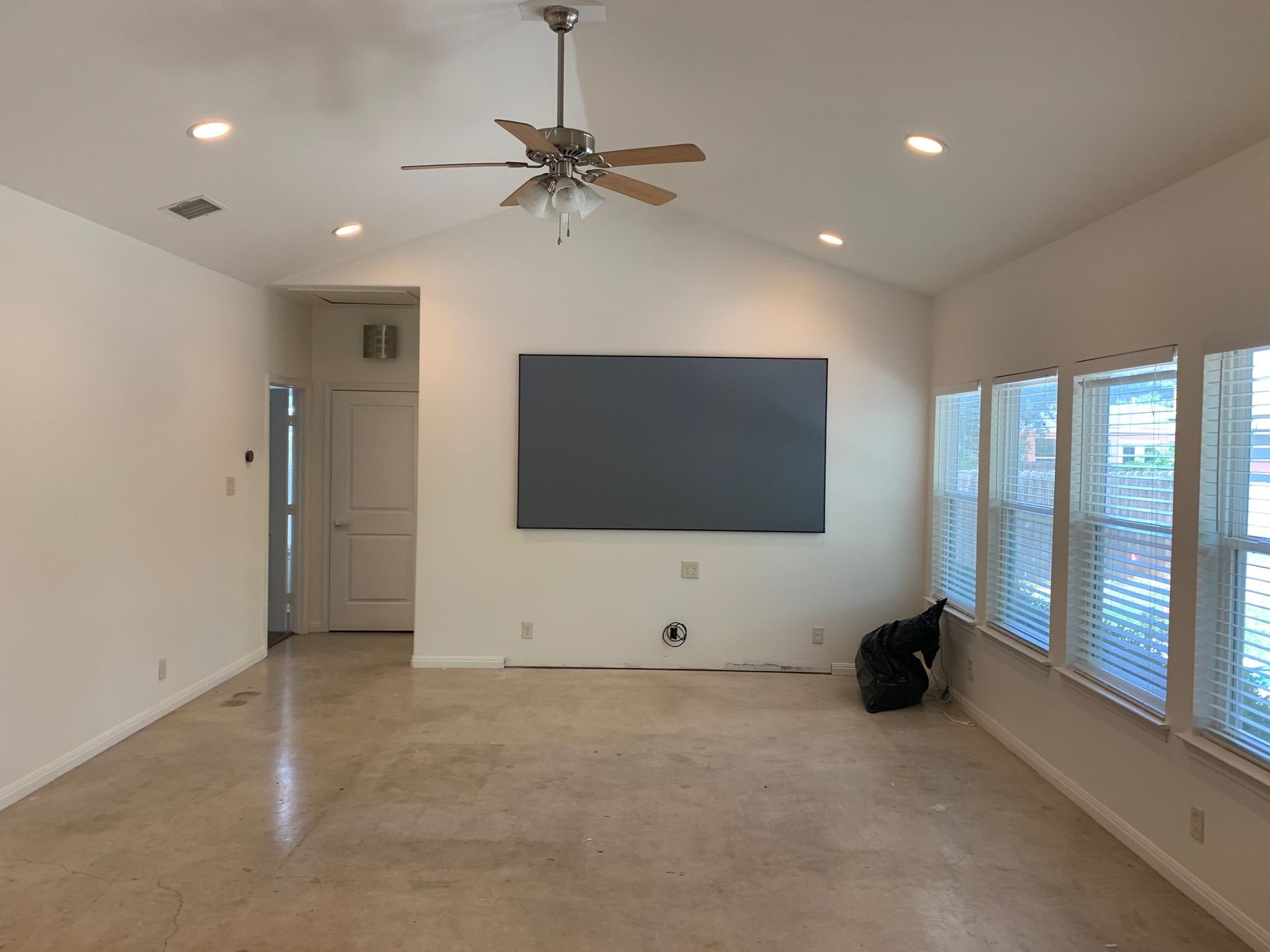 An empty living room with a ceiling fan and a flat screen tv on the wall.
